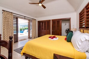 A hotel room with a bed, a ceiling fan, a view of the pool, and a door leading to another room.