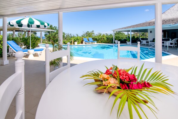 A poolside area with a table, lounge chairs, and a covered seating area.