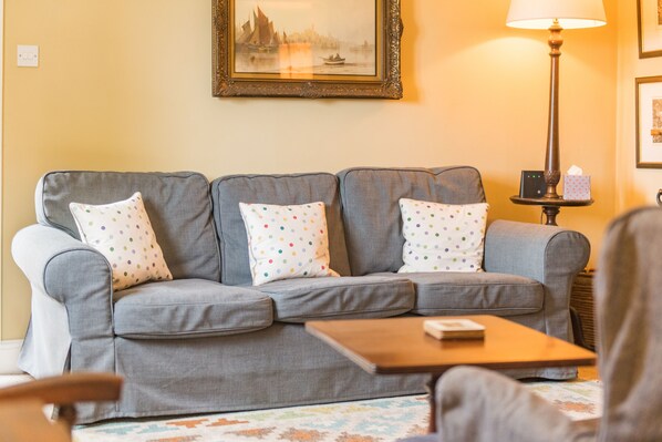 A living room with a grey sofa, colorful polka dot cushions, a wooden coffee table, a lamp, and a framed picture on the wall.