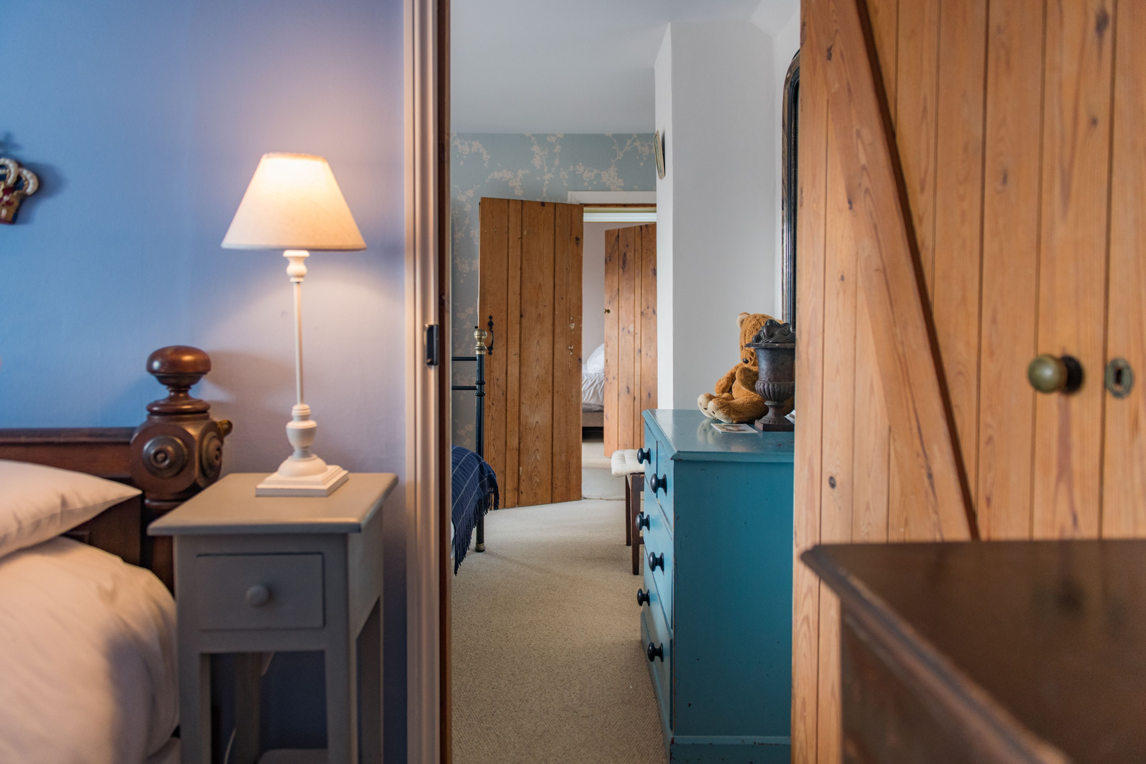 A bedroom with a bed, bedside table with a lamp, a dresser, and a wooden door.