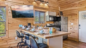 A wooden cabin interior with a kitchen area featuring a large TV, wooden cabinets, a refrigerator, and a bar with stools.