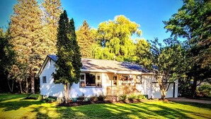A single-story house with a front porch, surrounded by trees and a well-maintained lawn. - Dog-Friendly Boyne City Home | Game Room, Near Lake Charlevoix + Downtown (Boyne City)
