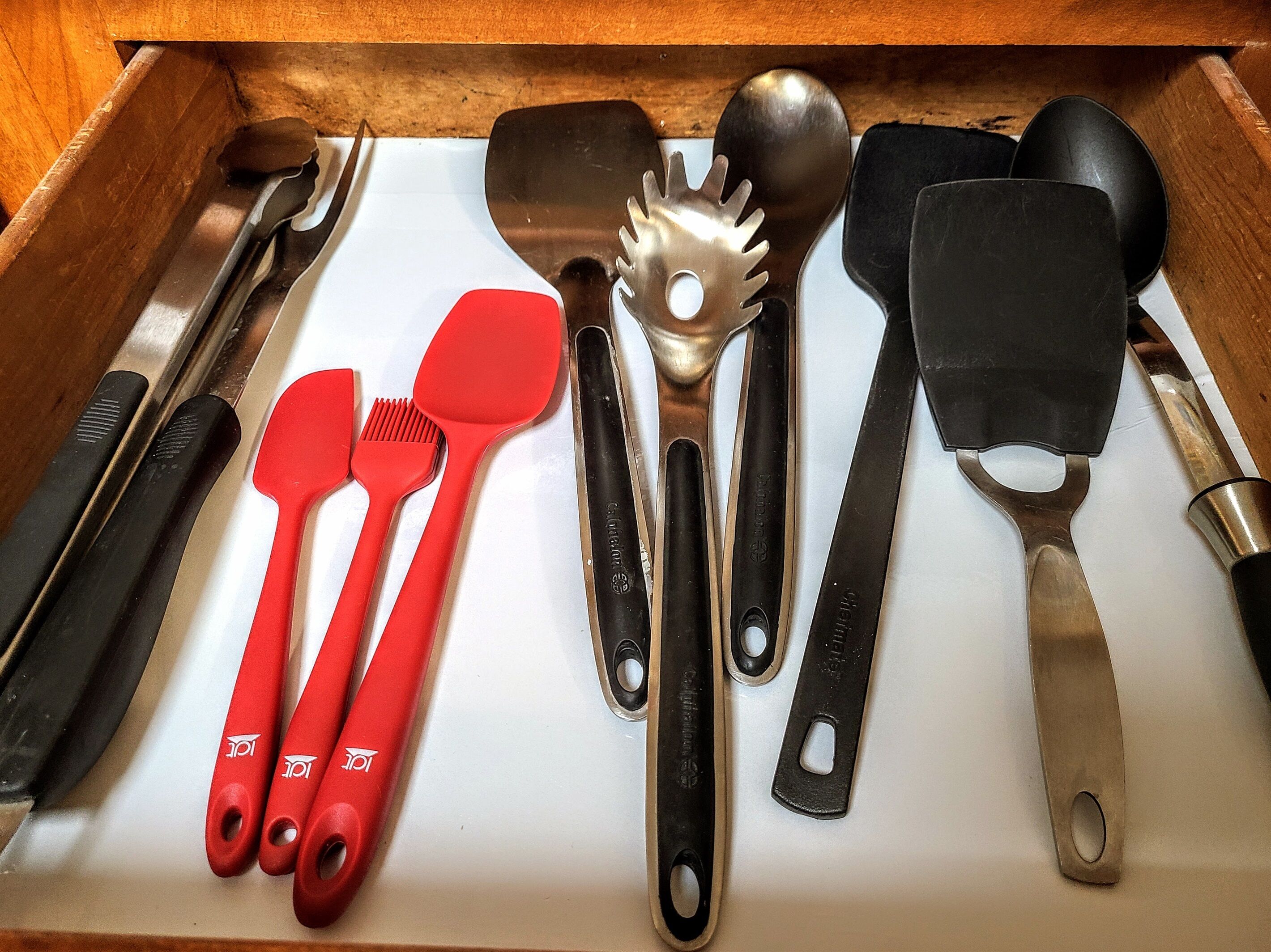 Un tiroir contenant divers ustensiles de cuisine, notamment des spatules, une louche et une râpe.