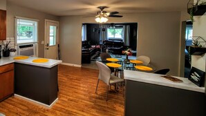 A modern kitchen with a central island, wooden flooring, and a dining area with yellow chairs and a small table. - Dog-Friendly Boyne City Home | Game Room, Near Lake Charlevoix + Downtown (Boyne City)