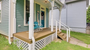 Eine Veranda mit Holzdeck, weißer Geländer und einer Treppe zum Eingang.
