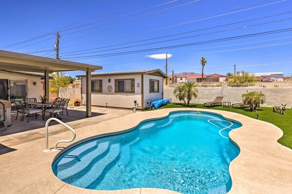 A swimming pool with a wavy edge, a covered patio area with outdoor furniture, and a small building with a sign. - 4 Mi to Lake Havasu: Luxe Home w/ Outdoor Oasis (Lake Havasu City)