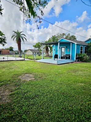 A blue house with a porch, surrounded by a grassy yard and palm trees. - Seahorse Suite Efficiency Apartment (Matagorda)