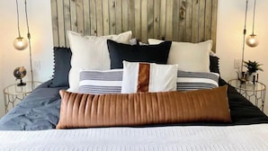 Ein Bett mit vielen Kissen, einem Holz-Kopfteil und zwei Nachttischlampen.