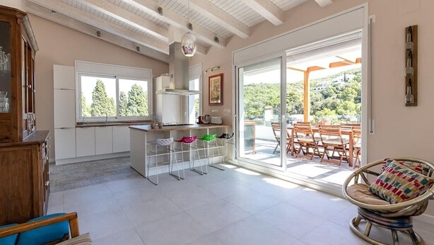 A modern kitchen with a central island, large windows, and a dining area with outdoor seating. - Villa Casa Nuestra with Private Pool, Garden & Wi-Fi (Begur)