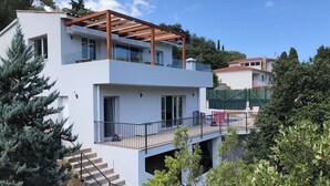 A modern two-story house with a balcony, a wooden pergola, and a staircase leading to the upper floor. - Villa Casa Nuestra with Private Pool, Garden & Wi-Fi (Begur)