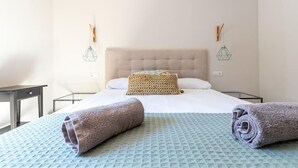 A hotel room with a bed, two bedside tables, a nightstand, a wall-mounted lamp, and a rolled towel on the bed. - Villa Casa Nuestra with Private Pool, Garden & Wi-Fi (Begur)