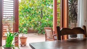 A patio area with a wooden table and chairs, surrounded by potted plants and a large tree. - Villa Rosso Corbezzolo (Carassai)