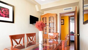 A dining area with a glass-top table, wooden chairs, a cabinet with glass doors, and a television mounted on the wall. - Holiday Apartment "El Refugio" with Wi-Fi & Terrace (Jerez de la Frontera)