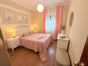 Una camera da letto con un letto, comodini, una sedia, una cassettiera, uno specchio e una finestra con tende.