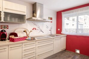 Cucina con mobili bianchi, cappa in acciaio inossidabile, parete rossa e finestra con vista sugli edifici.