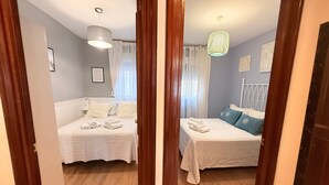 A bedroom with two beds, a wooden floor, a white ceiling, and a hanging light fixture. - Holiday Apartment "El Refugio" with Wi-Fi & Terrace (Jerez de la Frontera)