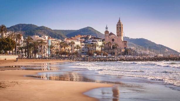 A coastal town with a prominent church, sandy beach, and a mountain in the background. - Apartment MariBeach Sitges with Terrace, A/C & Wi-Fi (Sitges)