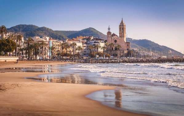 A coastal town with a prominent church, sandy beach, and a mountain in the background.