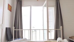 A bedroom with a bed, curtains, a chair, and a window. - Apartment MariBeach Sitges with Terrace, A/C & Wi-Fi (Sitges)