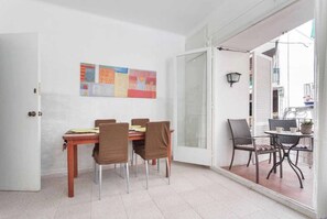 Un espace repas comprenant une table et des chaises, un tableau abstrait aux couleurs vives, une porte-fenêtre coulissante et un petit coin salon extérieur avec une table et des chaises.