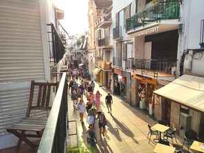 A crowded street with people walking, shops, and buildings with balconies.