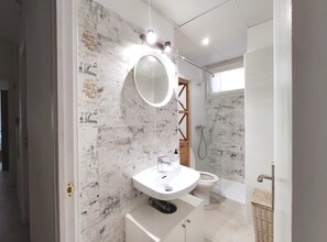 A bathroom with a round mirror, white sink, and a shower area.