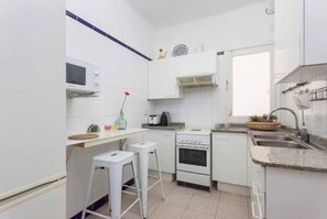Una cocina compacta con armarios blancos, un microondas, una estufa y un lavabo.
