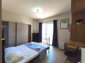 A bedroom with a bed, a desk, a chair, a wardrobe, and a window with curtains.
