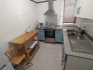 A compact kitchen with a microwave, stove, sink, and a wooden table with a chair.
