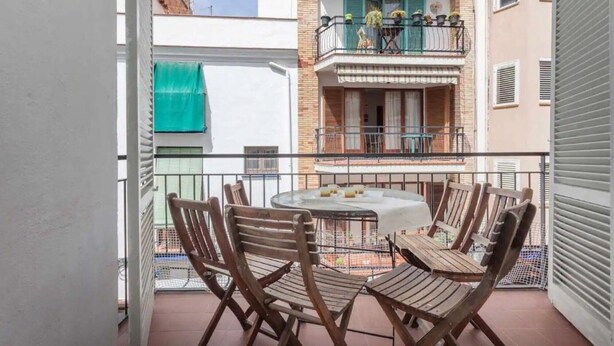 Un balcon avec une table ronde et quatre chaises en bois, une vue sur un immeuble doté d’un balcon et une marquise verte.
