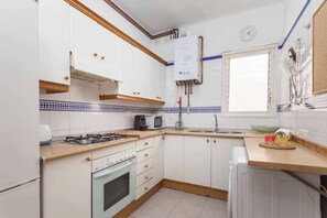 A kitchen with white cabinets, a stove, a microwave, and a window.