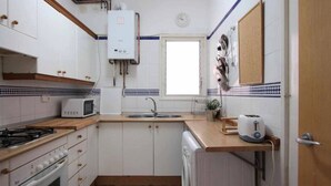 A compact kitchen with white cabinets, a built-in stove, a microwave, a sink, and a window. - Holiday Home 'Maribeach3' with Private Terrace, Wi-Fi and Air Conditioning (Sitges)