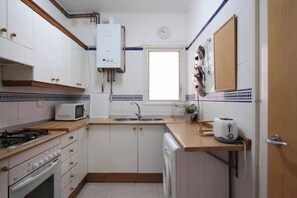 Una cocina compacta con armarios blancos, estufa integrada, microondas, fregadero y ventana.
