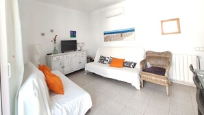 A room with a bed, a sofa, a wicker chair, a TV on a cabinet, and a wall-mounted air conditioner. - Holiday Home 'Maribeach3' with Private Terrace, Wi-Fi and Air Conditioning (Sitges)