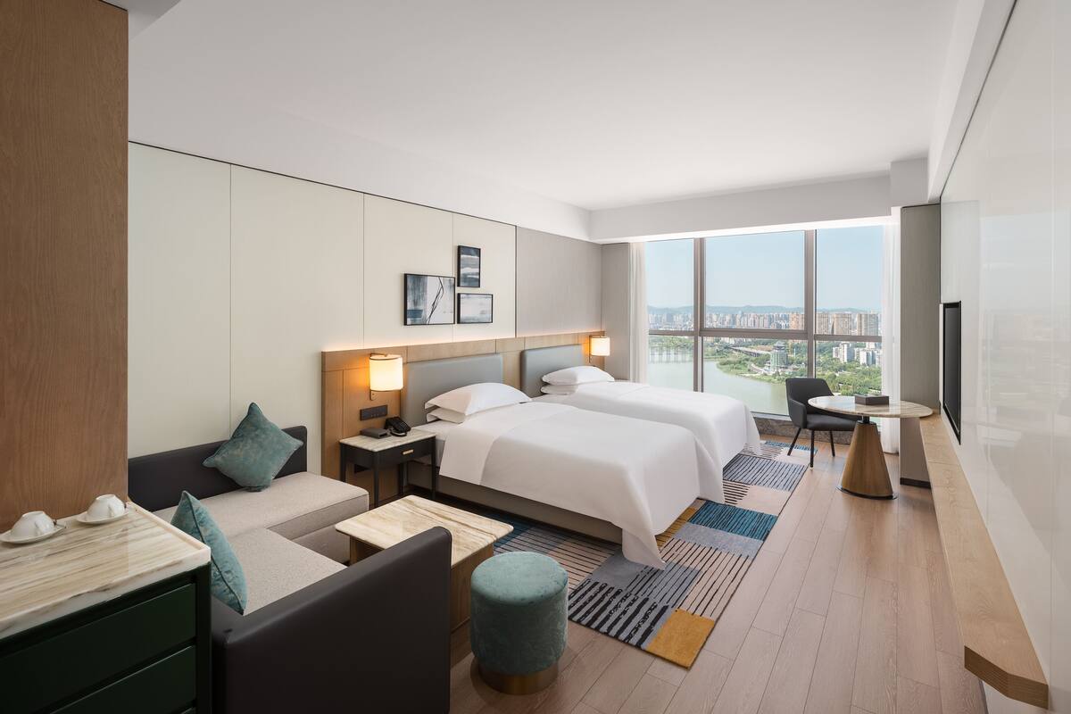 A modern hotel room with a large bed, bedside tables, a desk, and a view of the city.