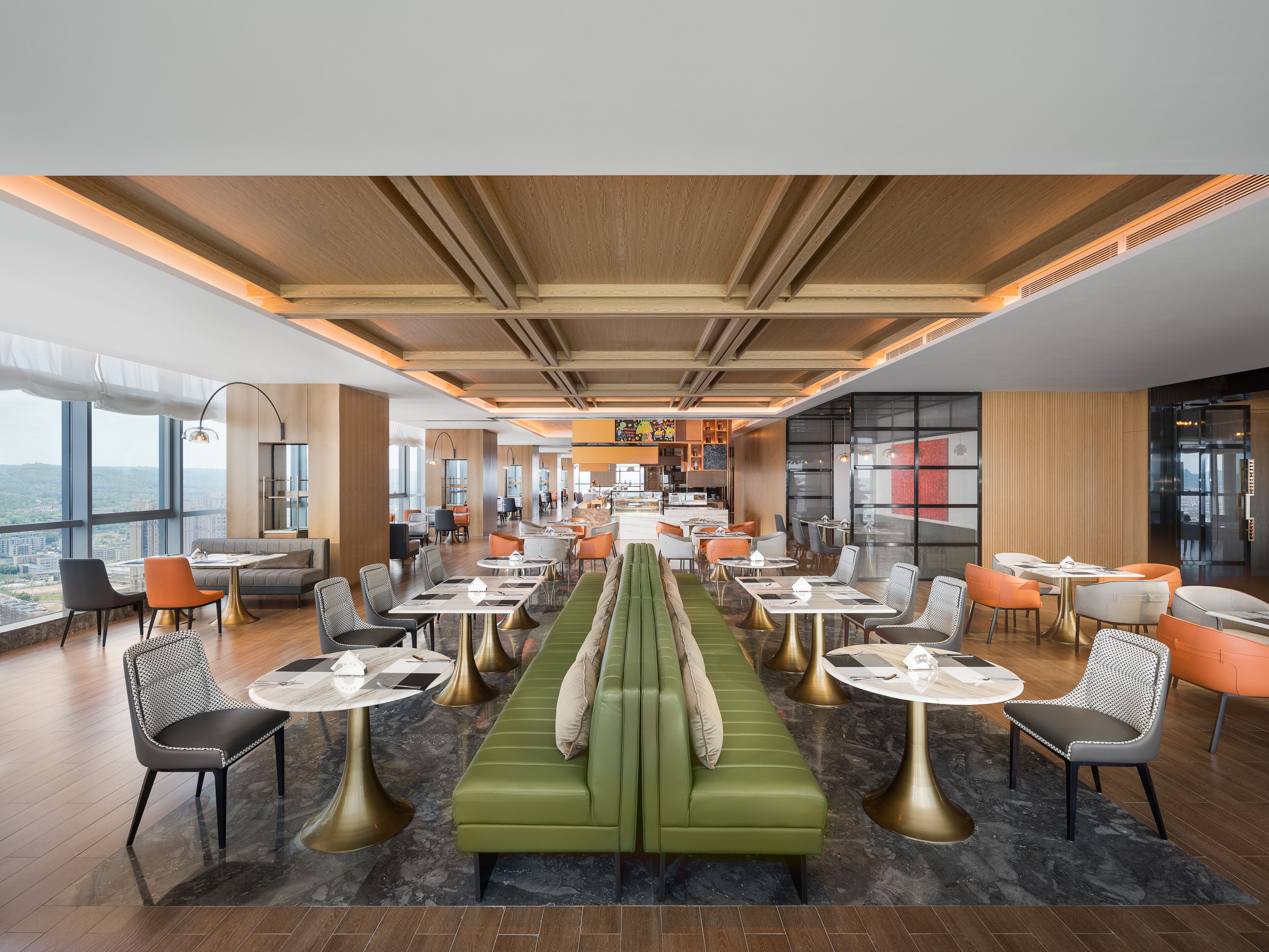En rymlig hotellobby med en stor, grön soffa i mitten, flera sittgrupper och utsikt över stadsbilden genom stora fönster.