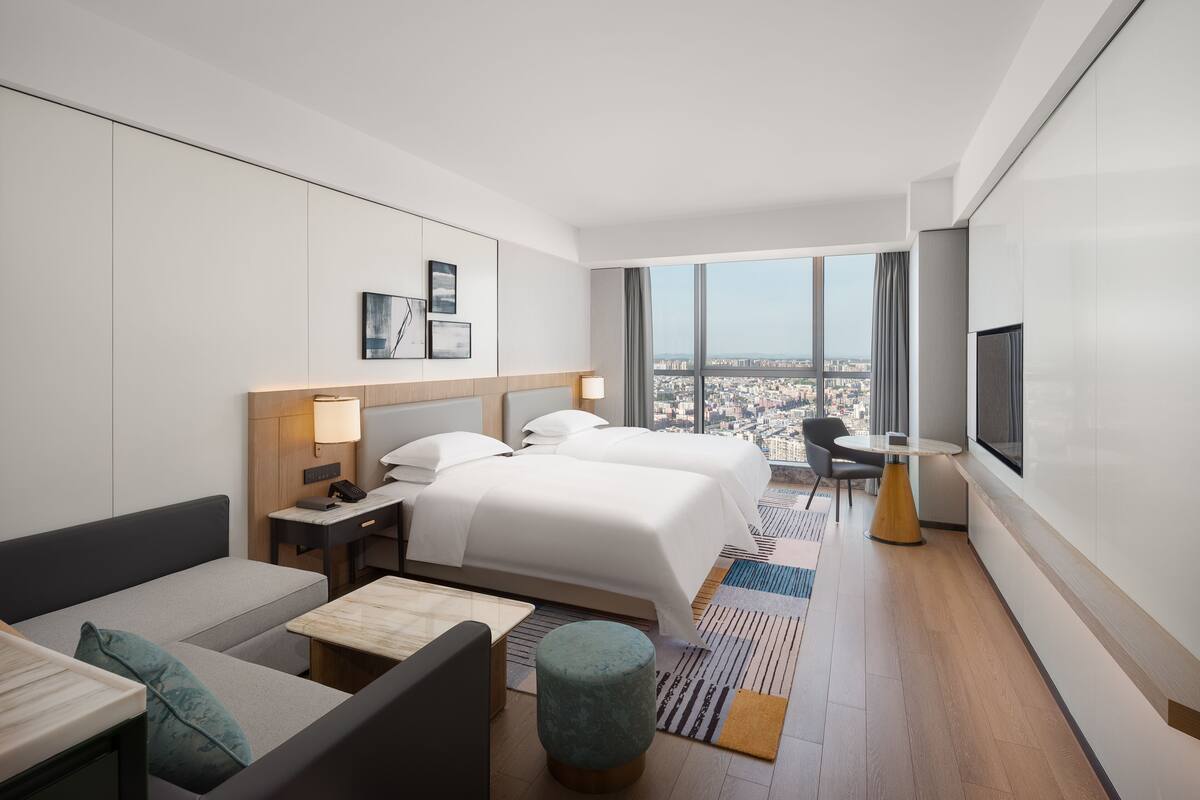 A modern hotel room with a large bed, a desk, a chair, and a TV.