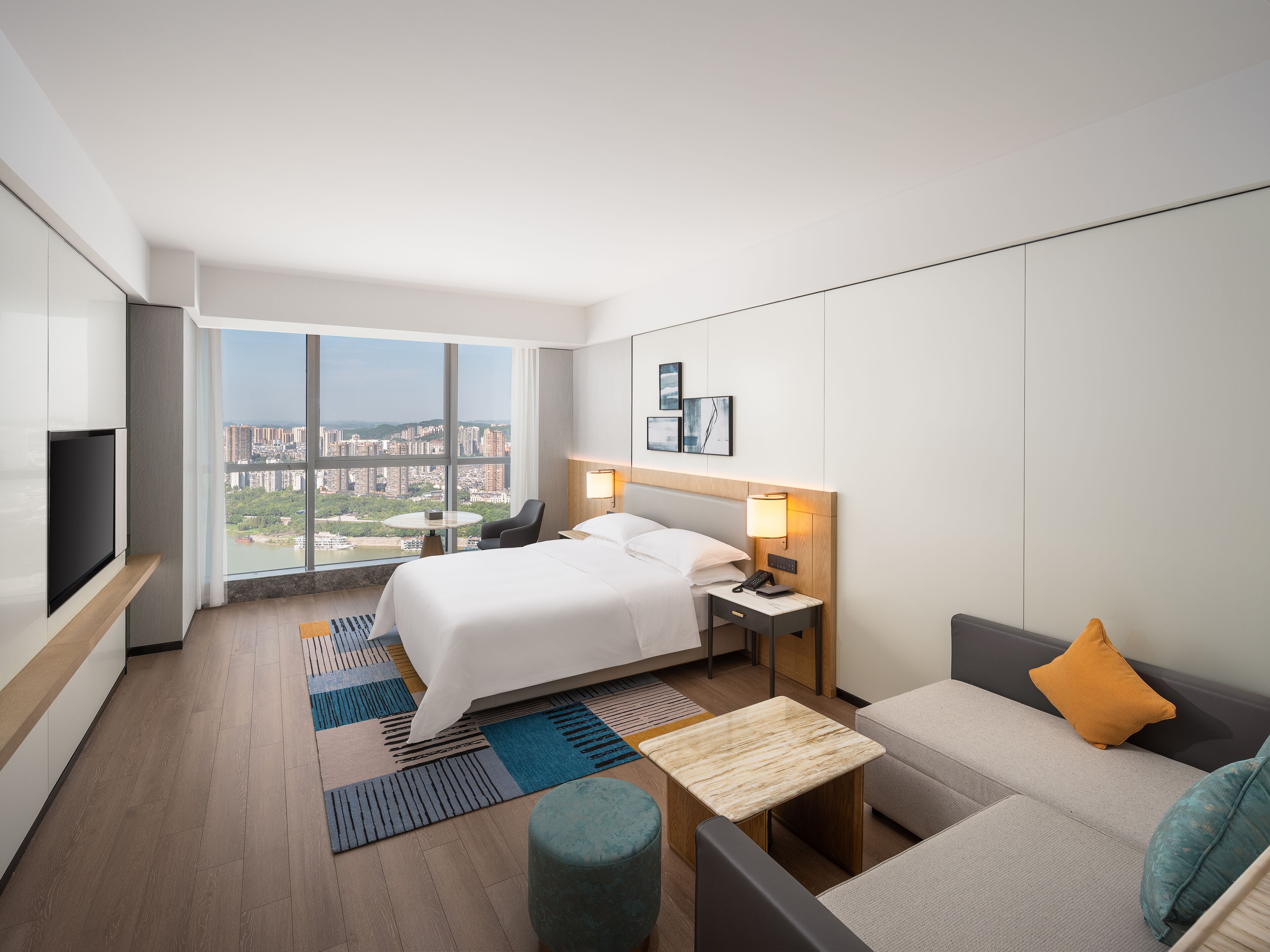Una habitación de hotel moderna con una cama grande, un sofá, una mesita, un televisor y vistas a la ciudad.