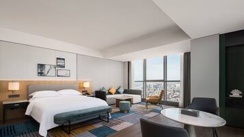 Una habitación de hotel moderna con una cama grande, un sofá, una mesita y vistas a la ciudad.