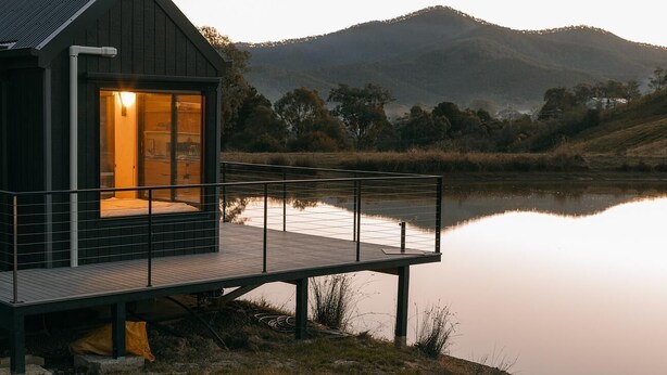 A modern cabin with a deck overlooking a calm lake and hills in the background. - Beautifully appointed Tiny House. (Goughs Bay)