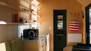 A compact kitchen with wooden shelves, a coffee maker, and a laptop on a table. - Beautifully appointed Tiny House. (Goughs Bay)