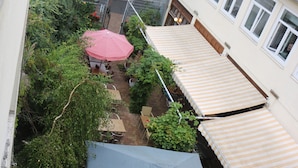 A courtyard with a covered seating area, a pergola, and a building with a striped awning. - Penthaus Am Köpcke (Hannover)