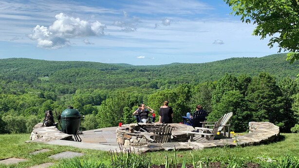 An outdoor seating area with stone tables and chairs, surrounded by lush greenery and a view of rolling hills. - Chef’s Kitchen, Fast Wi-Fi (Hillsdale)
