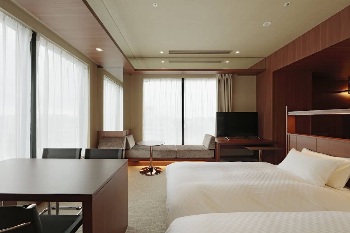 A hotel room with a bed, a desk, a chair, a sofa, and a television.