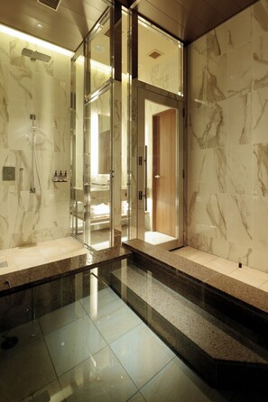 Une salle de bain moderne dotée d’une douche à parois de verre, de murs en marbre et d’un banc intégré.