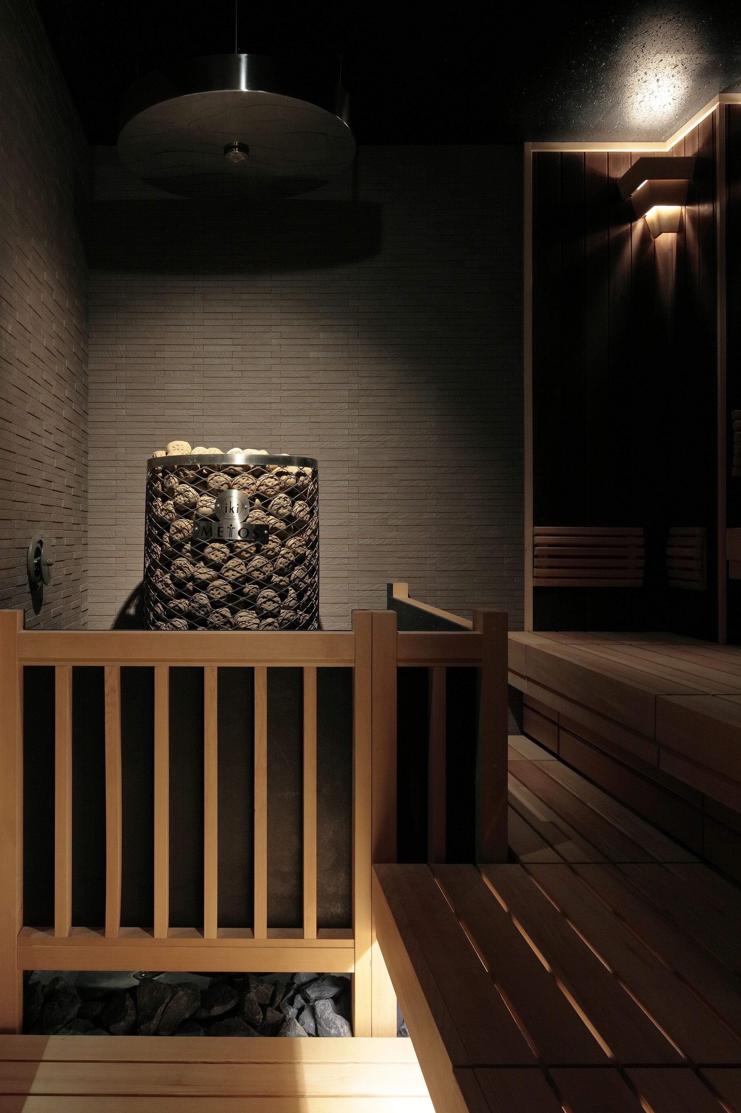 Una sauna con un banco de madera, pared de piedra y una lámpara colgante.