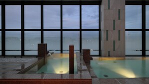 A modern indoor pool with clear glass walls, a stone floor, and a view of the city skyline. - Candeo Hotels Kumamoto Shinshigai (Kumamoto)