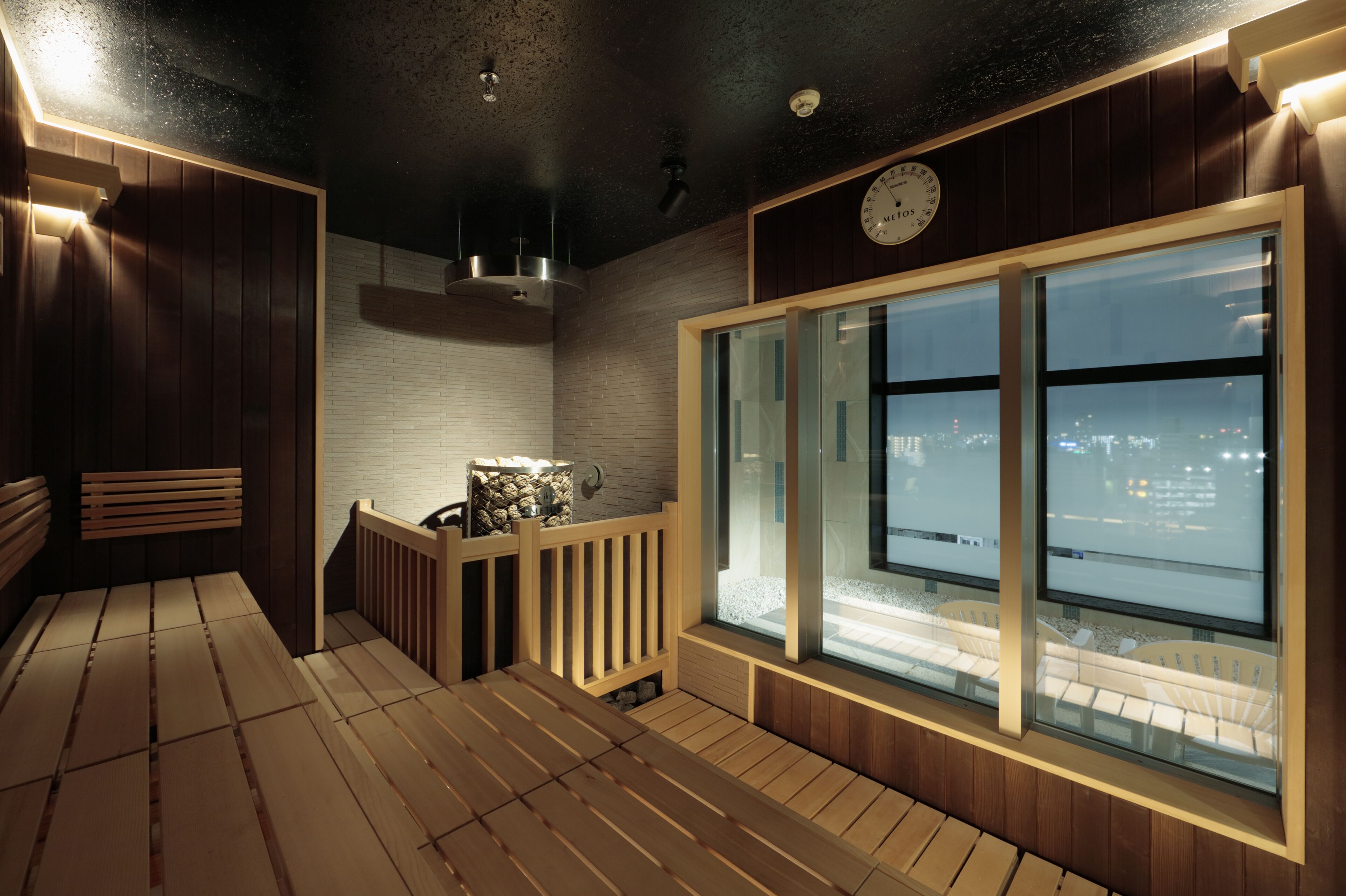 Een sauna met houten banken, een stenen kuip en een groot raam met uitzicht op de stad.