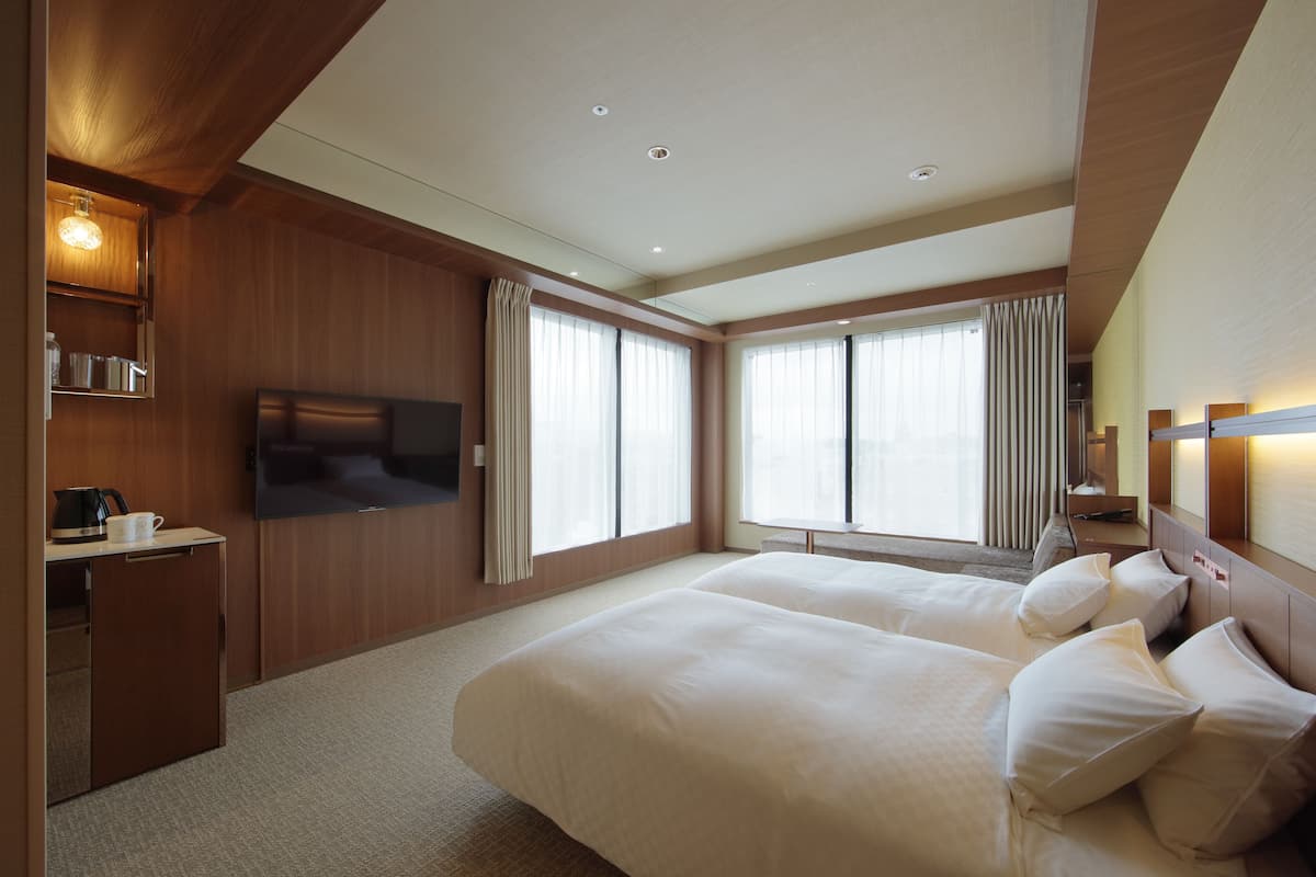 A hotel room with a large bed, a TV mounted on the wall, a desk with a coffee maker, and a window with curtains.