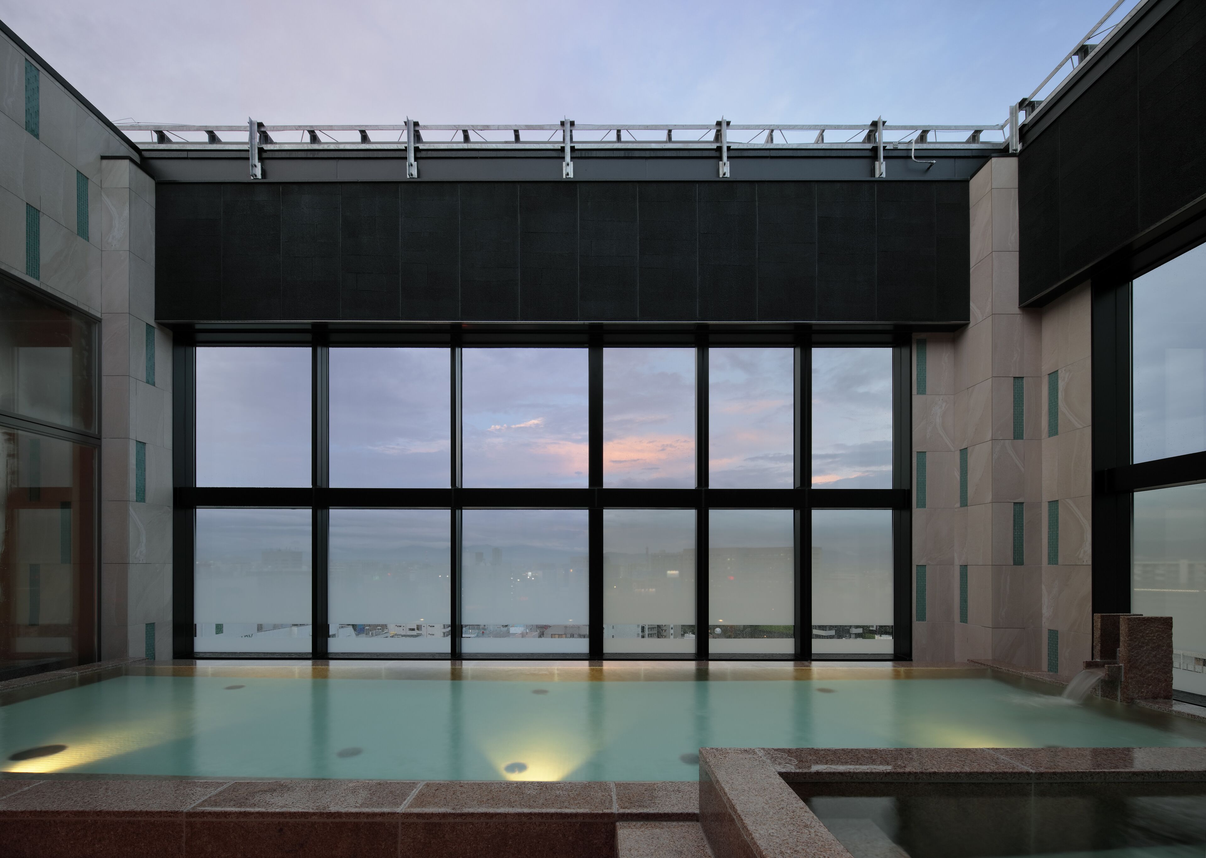 A modern indoor swimming pool with large windows offering a view of the cityscape.